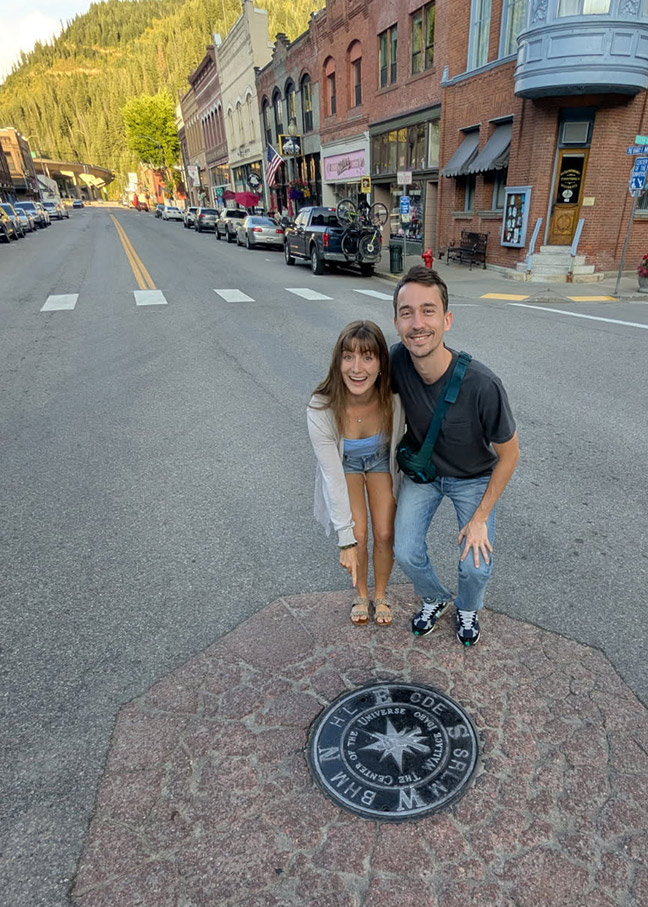 Sierra Bradtz and her partner standing next to a plaque that says "the center of the universe" in Wallace, ID